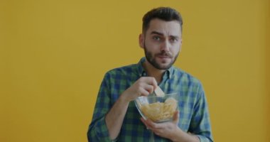 Patates cipsi yiyen ve sarı arka planda televizyon seyreden neşeli bir adamın portresi. İnsanlar ve yaşam tarzı kavramı.