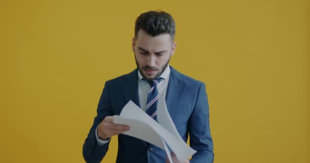 いらいらする従業員の肖像は ビジネス文書を読んでから紙を投げ 黄色の背景に笑顔 人と書類の概念 — ストック動画