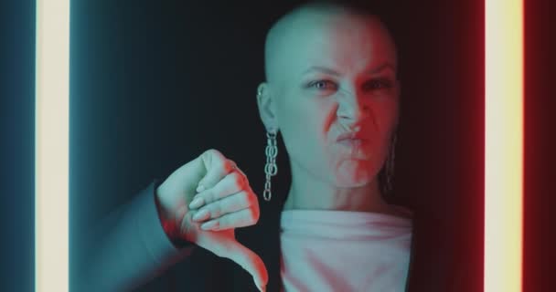輝くネオンの背景に親指を手ジェスチャーを作る不幸な若い女性のクローズアップ肖像画 否定的な感情と失望の概念 — ストック動画