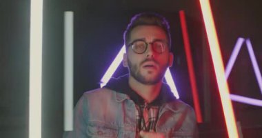 Neon ışıklı arka planda dans eden genç ve mutlu bir kulüp üyesinin yavaş çekim portresi. Eğlence ve tasasız milenyum konsepti.
