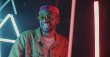 Şık kıyafetler içinde dans eden ve parlak neon arka planda el kol hareketleriyle hareket eden heyecanlı bir adam. Modern gençlik ve eğlence konsepti.