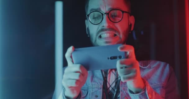 Kerl Mit Kopfhörer Spielt Videospiel Mit Smartphone Auf Neonlicht Hintergrund — Stockvideo