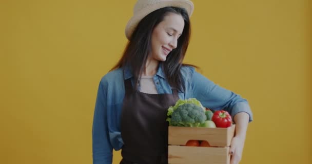 一位年轻女子的画像 她拿着装有新鲜蔬菜的盒子 黄色背景上有有机的养殖标志 健康营养和耕作概念 — 图库视频影像