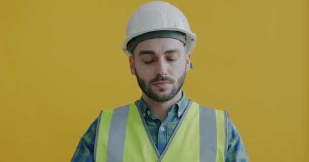 黄色の背景だけに立ってテープメジャーを使用して安全均一なビルダーの肖像画 建設労働者及び設備概念 — ストック動画