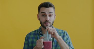 Smoothie içen genç adamın yavaş çekimde portresi. Sarı arka planda sağlıklı içkinin tadını çıkarıyor. İnsanlar ve beslenme konsepti.