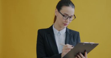 Takım elbiseli genç bir iş kadınının portresi sarı arka planda belgelerle çalışıyor. Okuma yazma bilen ve elinde kağıt tutan bir kadın..