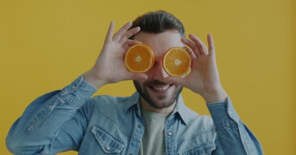 年轻男子用橙子遮住眼睛 在黄色背景下做笑脸的慢动作肖像画 水果与幸福概念 — 图库视频影像