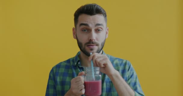 黄色の背景で味と健康的な飲み物を楽しんでスムージーを飲む若い男のスローモーションの肖像画 人々と栄養の概念 — ストック動画