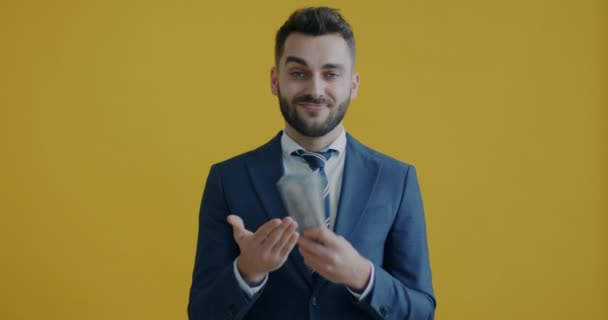 成功した起業家のスローモーションの肖像は 銀行券を投げ 黄色の背景に笑みを浮かべてお金を保持 経営の考え方 — ストック動画