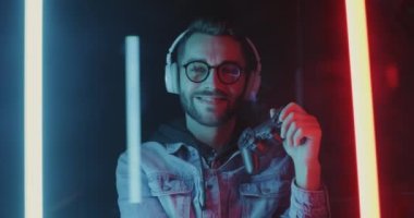 Kulaklık ve joystick 'li çekici bir adamın yavaş çekim portresi. Parlak neon ışıklı arka planda duruyor. İnsanlar ve gece hayatı kavramı.