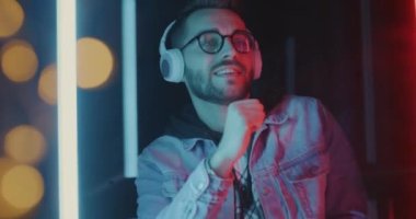 Dertsiz dans eden öğrencinin renkli ışıklı arka planda kulaklıkla müzik dinlemesinin zevkini çıkarması. Eğlence ve gelecekçi kültür kavramı.
