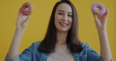 Donutlarla oynayan ve sarı arka planda sevimli suratlar yapan çekici genç bir bayan portresi. Lezzetli tatlı ve insanlar konsepti.