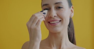 Çekici bir kadının yüzüne süngerle dokunup sarı arka plana makyaj yaptığı yakın plan portresi. Deri bakımı ve kozmetik konsepti.