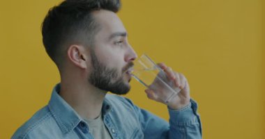 Camdan su içen yakışıklı genç adam sarı arka planda sağlıklı içkinin tadını çıkarıyor. Yenileme ve beslenme kavramı.