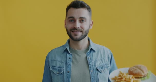 年轻人在健康蔬菜沙拉和黄色背景微笑之间选择快餐汉堡和薯条的肖像 青年生活方式和营养概念 — 图库视频影像