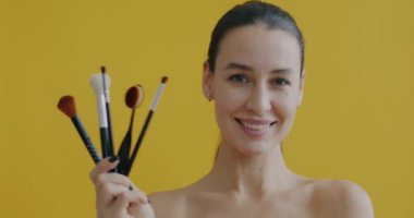 Sarı arka planda gülümseyen güzel bayan makyaj fırçaları setinin yavaş çekim portresi. Kozmetik aletler ve güzellik ürünleri konsepti.