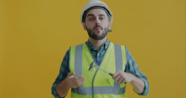 Sarı arka planda çekiçle eğlenen genç bir inşaat işçisinin portresi. Profesyonel araçlar ve endüstriyel üniforma konsepti.