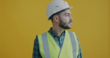 Güvenlik üniformalı genç adamın yavaş çekimde kameraya dönüp miğfere dokunarak inşaata hazır olması. Meslek ve insan kavramı.