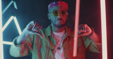 Afro-Amerikan bir adamın neon arka planda aşağılayıcı davranışlar gösteren yavaş hareket portresi. İnsanlar ve olumsuz duygu kavramı.