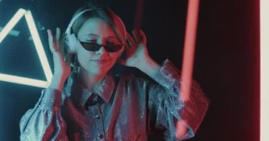 Neon ışıklı alanda şarkı söyleyen ve dans eden kulaklıklarla müzik dinleyerek eğlenen kız öğrenci portresi. Eğlence ve yaratıcı gençlik kavramı.