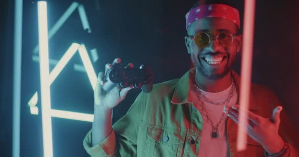 Πορτρέτο Του Χαρούμενου Αφροαμερικανού Gamer Δείχνοντας Χειριστήριο Και Χαμογελώντας Neon — Αρχείο Βίντεο