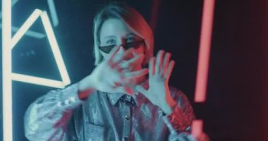 Tasasız öğrenci portresi, modaya uygun kıyafetler içinde karanlık neon ışıklı alanda dans ediyor, müzikten zevk alıyor. İnsanlar ve eğlence kavramı.