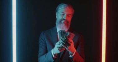 Müsrif iş adamının para saçan ve kara neon arka planda duran yavaş hareket eden portresi. Halk ve finans kavramı.