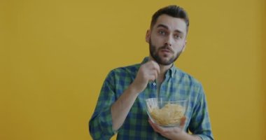 Patates cipsi yiyen ve sarı arka planda kameraya bakan genç adamın portresi. Atıştırmalık ve boş zaman konsepti.