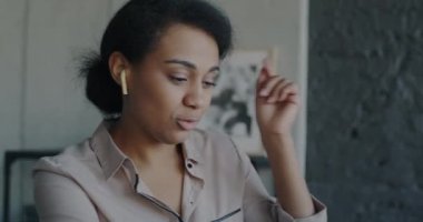 Neşeli bir Afro-Amerikan çalışanı müzik dinliyor ve modern ofiste dizüstü bilgisayarla çalışıyor. İş molası ve gençlik kültürü konsepti.