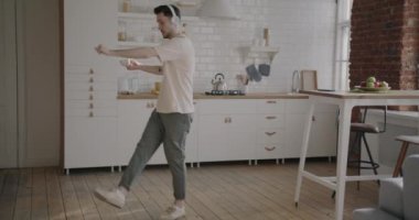 Tasasız genç adam bir fincan kahveyle dans ediyor ve mutfakta müzik dinliyor. Modern yaşam tarzı ve boş zaman aktivitesi konsepti.