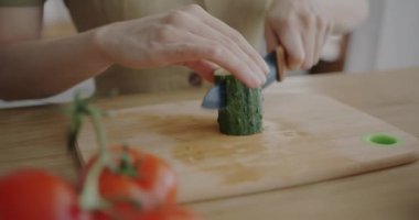 Kadın eli, mutfak masasında salatalık kesen sebze salatası hazırlıyor. Organik gıda ve sağlıklı yemek konsepti.