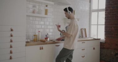 Modern mutfakta dans eden, kahve içen ve akıllı telefon kullanan mutlu adam. Çağdaş teknoloji ve gençlik kavramı.