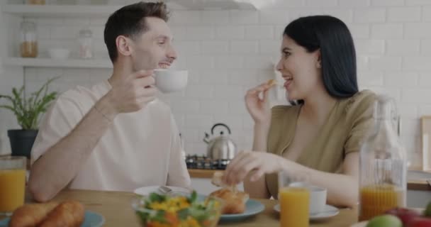 男人和女人在厨房的公寓里一边喝咖啡一边笑着吃羊角面包 共进早餐和家庭生活方式概念 — 图库视频影像