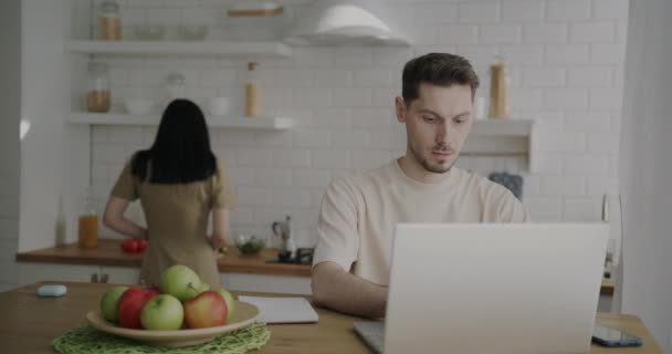 年轻人在大流行期间在家工作 一边用笔记本电脑 一边在厨房做饭 家庭生活方式和遥远的工作概念 — 图库视频影像