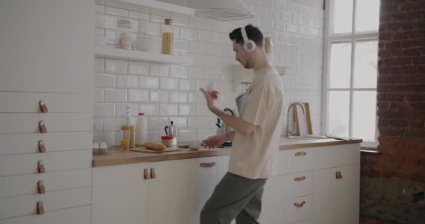 快乐的家伙跳舞喝咖啡和使用智能手机在现代厨房在家里 当代技术与青年人概念 — 图库视频影像