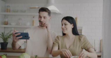 Mutlu çiftin portresi yemekle birlikte selfie çekiyor akıllı telefon kullanarak evde birlikte eğleniyorlar. Modern teknoloji ve ilişki kavramı.