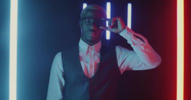 Ciddi bir iş adamı portresi bardak tamir ediyor sonra gülüyor ve sabun köpüğü tabancası ateşliyor siyah arka planda neon lambalarla eğleniyor. İş insanları ve rahatlama kavramı.