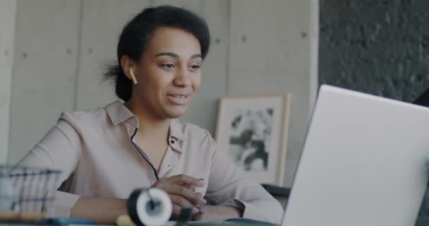 在虚拟会议期间 非裔美国女商人在办公室使用笔记本电脑 一边说话一边挥手 从办公室打网上视频电话的妇女 — 图库视频影像