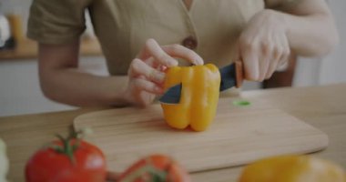 Kadın elinin taze biber pişirme salatasını keserek mutfak masasında sağlıklı bir yemek yaptığı yakın plan. Beslenme ve vejetaryen diyet konsepti.