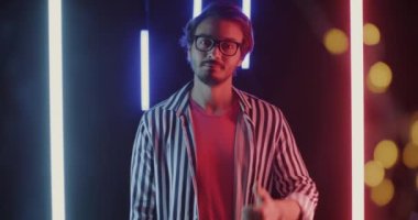 Neon ışıklarıyla arka planda mutluluğu ifade eden baş parmaklarını kaldıran neşeli genç adamın yavaş hareket eden portresi.