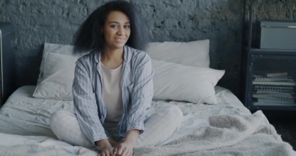 身穿睡衣的快乐的非洲裔美国女人的画像转向镜头 微笑着坐在卧室的床上 休闲和积极情绪概念 — 图库视频影像