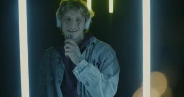 Kulaklık takan, müzikten hoşlanan ve neon ışıkta dans eden genç adamın yavaş çekim portresi. İnsanlar ve sigara konsepti.