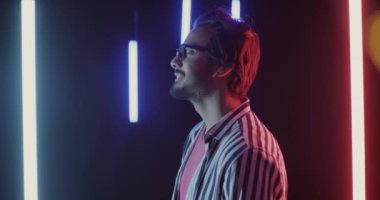 Kablosuz kulaklıkla müzik dinleyen genç bir adamın yan görüntüsü. Siyah arka planda neon ışıklı dans ediyor. Eğlence konsepti için insanlar ve modern teknoloji.