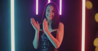 Yavaş çekimde mutlu bir kadın el çırpıyor ve kameraya bakıp neon arka planda memnuniyetini ifade ediyor. Pozitif duygu ve insanların kavramı.