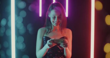 Siyah arka planda akıllı telefonlu, neon ışıklı, çevrimiçi video oyunu oynayan tatlı bir kız. İnsanlar ve eğlence konsepti.