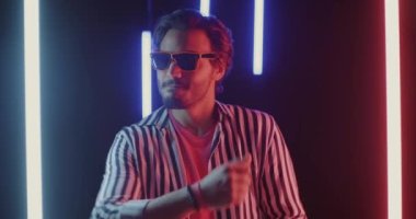 Gece kulübünde ışıklı gözlüklü neon lambalarla dans eden neşeli bir adamın yavaş çekim portresi. Kulüp ve gece hayatı kavramı.