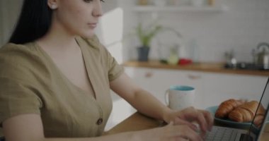 Evdeki mutfakta dizüstü bilgisayarla çalışan hırslı genç bir kadın. Uzak iş ve iş konsepti için modern teknoloji.
