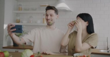 Akıllı telefonlu komik selfie çeken neşeli gençler mutfakta birlikte gülüp eğleniyorlar. Gençlik yaşam tarzı ve fotoğraf konsepti.