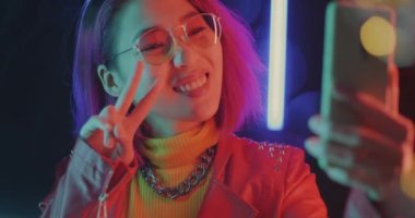 Çok renkli neon arka planda gülümseyen akıllı telefon kamerasıyla selfie çeken mutlu Asyalı kadın portresi. Gençlik ve modern teknoloji kavramı.