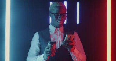 Afrika kökenli Amerikalı iş adamının portresi. Akıllı telefon ve içkiyle karanlık uzayda neon ışıklı kahve içmeye gidiyor. Modern teknoloji ve kurumsal yaşam tarzı kavramı.